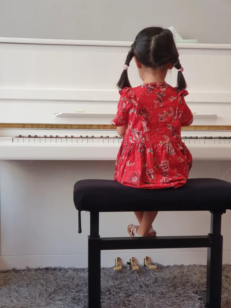Jeune élève assise devant un piano blanc pendant son apprentissage
